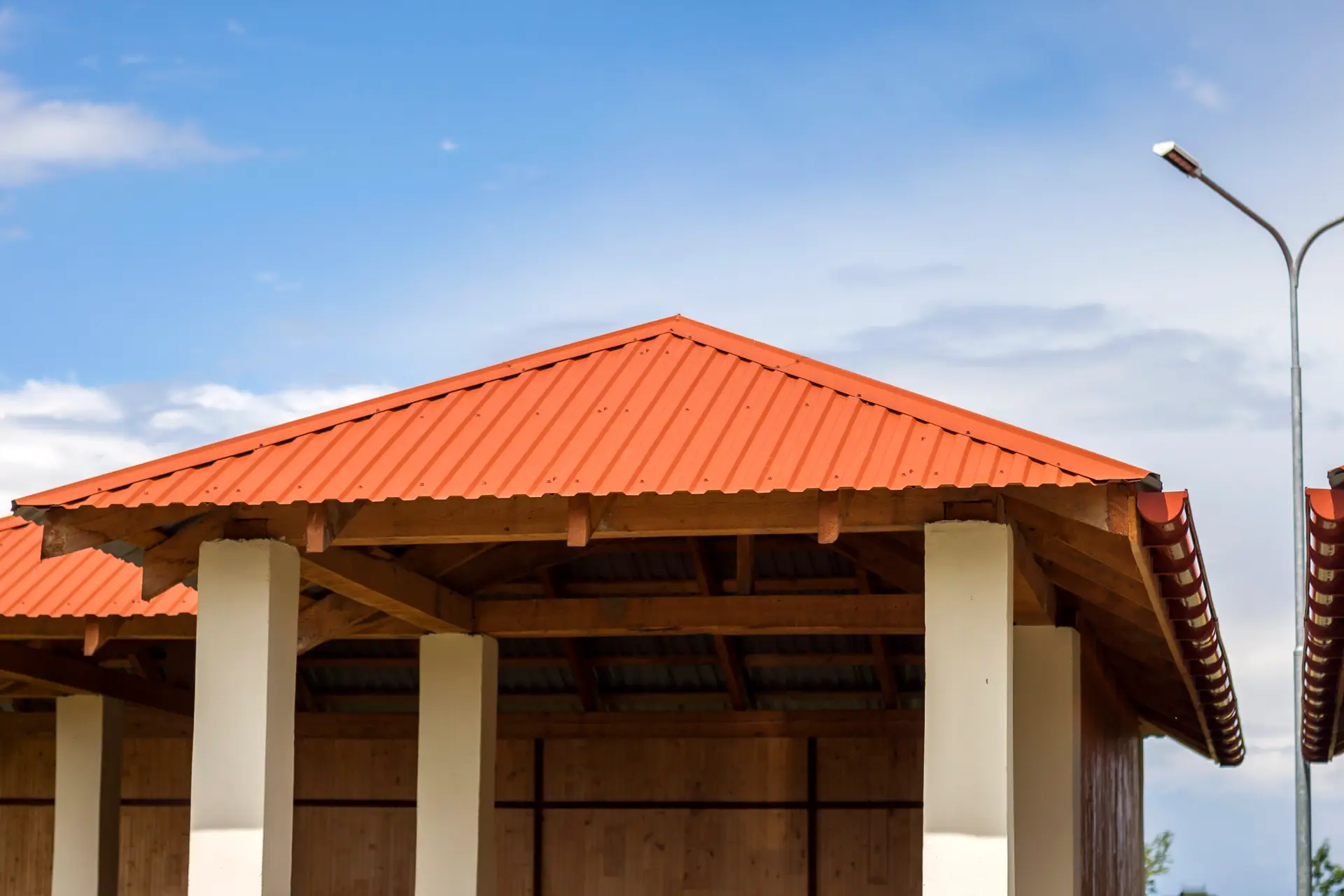 Close-up detail view of beautiful new modern alcove on kindergarten playground with bright orange tiling roof on clear blue sky background. Perfect place for children activities outdoors.